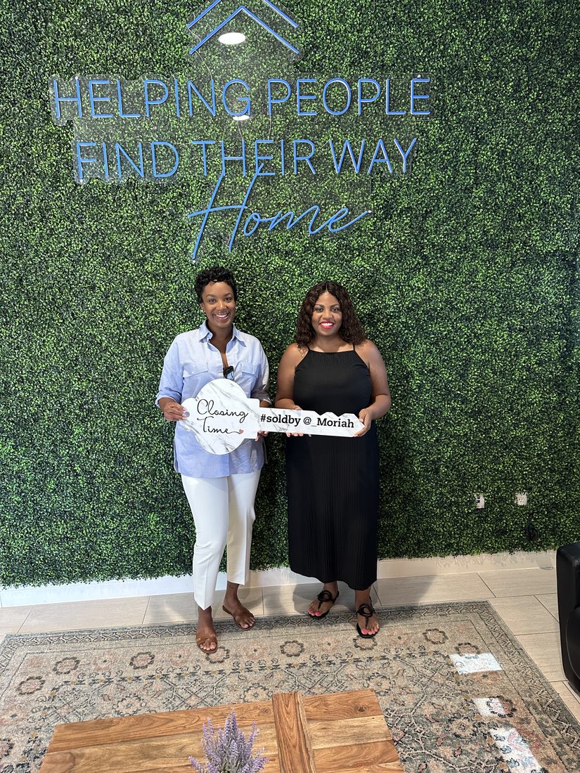 Two clients holding a Diversify Real Estate Group closing sign at a title company office